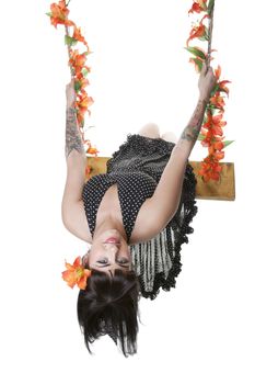 A carefree, Rockabilly pinup girl swinging on a tigerlily entwined rope swing.  Shot on white background.