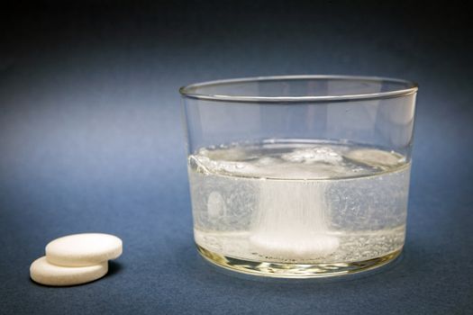 effervescent tablet into glass of water isolated on blue