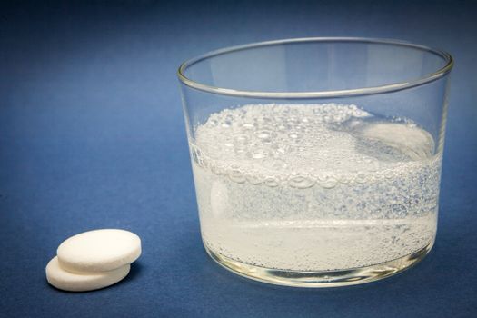 effervescent tablet into glass of water isolated on blue
