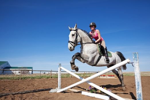 A beautiful, dappled gray horse with rider,  jumping a hurdle.