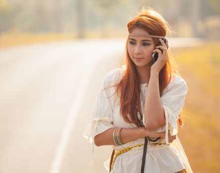 Beautiful young hippie girl using mobile phone on the country road