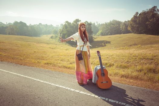 Hippie girl with guitar hitchhiking on countryside road