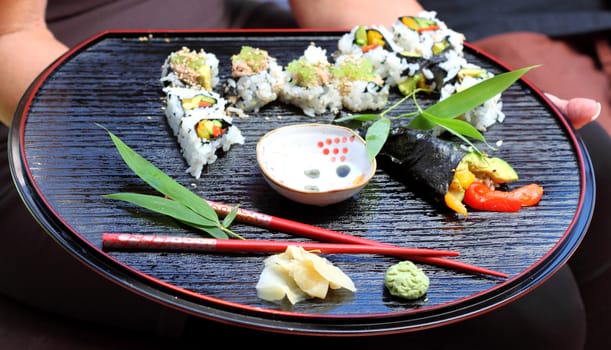Nicely decorated presentation of sushi on a black serving plate.