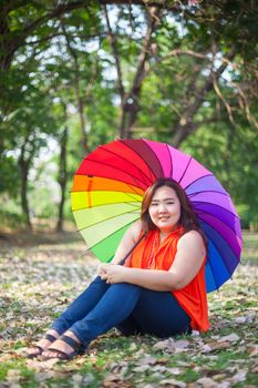 Young asian fat woman sitting with umbrella in autumn park