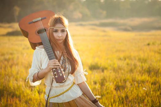 Hippie woman walking in golden field with acoustic guitar