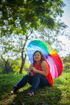 Young asian fat woman sitting with umbrella in autumn park