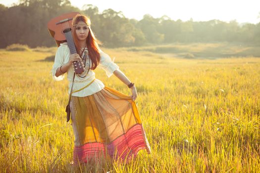 Hippie woman walking in golden field with acoustic guitar