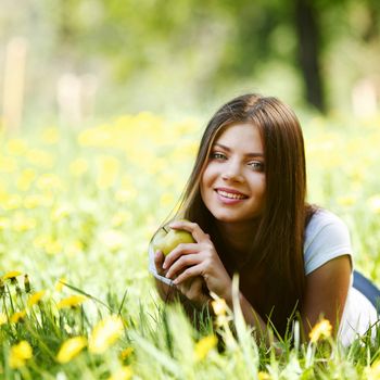 Young beautiful woman with apple resting on fresh green grass with flowers