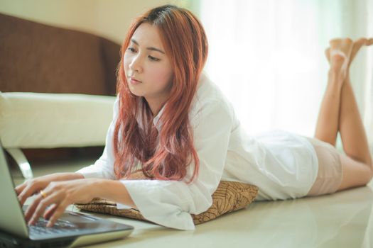 Happy asian young woman lying using laptop at home