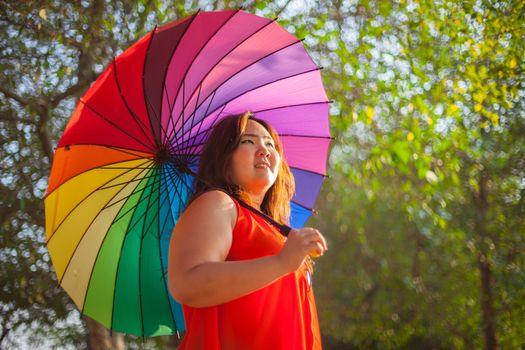 Happy fatty asian woman with umbrella outdoor in a park