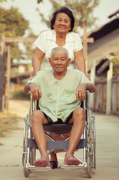 Asian senior woman pushing her disabled hasband on wheelchair