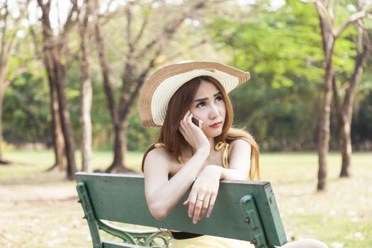 Woman talking on phone Sitting on a wooden bench in the park.