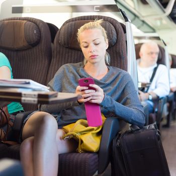 Thoughtful young lady surfing online on smartphone while traveling by train.