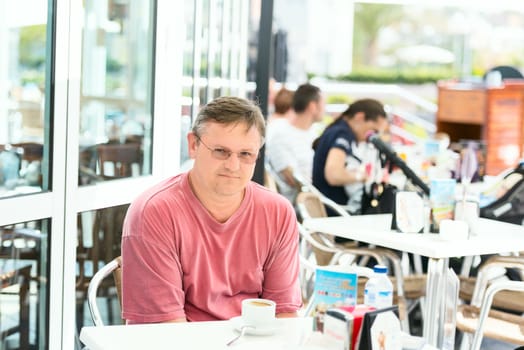 Middle aged men in red t-shirt drinking coffee at outdoor cafe