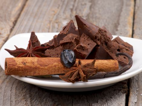 Dark Chocolate Pieces with Cinnamon Stick, Vanilla Pod and Anise Stars on White Plate isolated on Wooden background