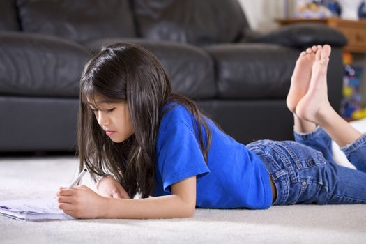 Little biracial Asian girl doing her homework on floor