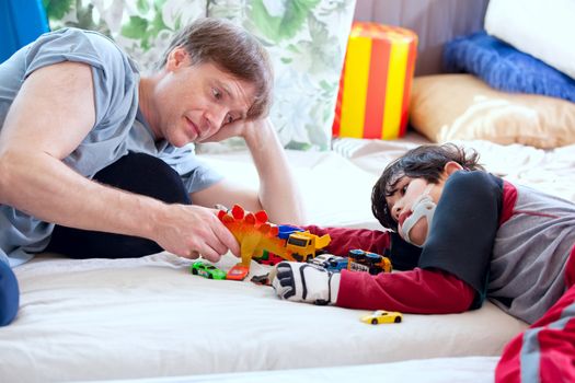 Handsome father playing cars with disabled son on floor mat