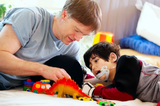 Handsome father playing cars with disabled son on floor mat