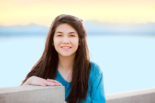 Beautiful biracial young teen girl enjoying outdoors by lake at sunset