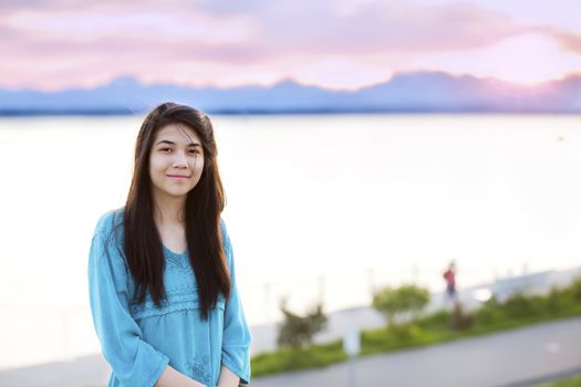 Beautiful biracial young teen girl enjoying outdoors by lake at sunset