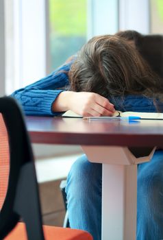 Tired student asleep at school table, head on book