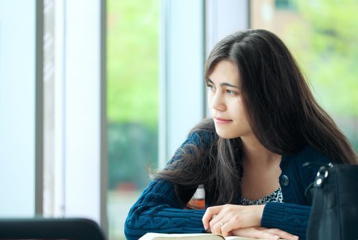 Tired young biracial  student looking out window while studying