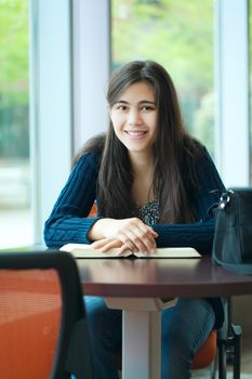 Happy young college student studying at school, book on table