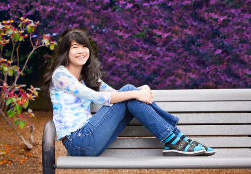 Young biracial preteen girl ejoying outdoors, sitting on wooden park bench