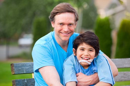 Handsome father sitting with smiling disabled seven year old son outdoors
