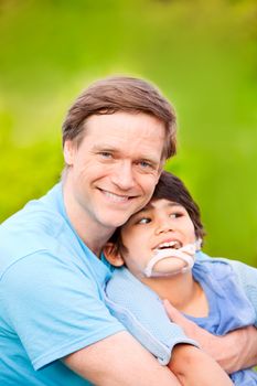 Handsome father sitting with smiling disabled seven year old son outdoors