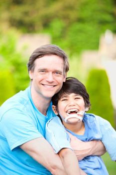 Handsome father sitting with smiling disabled seven year old son outdoors