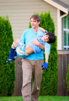 Father carrying disabled seven year son outdoors