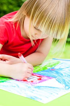 Little girl sitting at table drawing a house outdoors