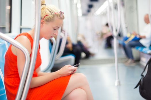 Beautiful blonde caucasian lady in red dress traveling by metro.