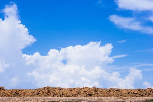 Red soil with blue sky and white clouds.