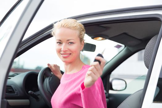 Woman driver showing car keys. Young female driving happy about her new car or drivers license. Caucasian model.