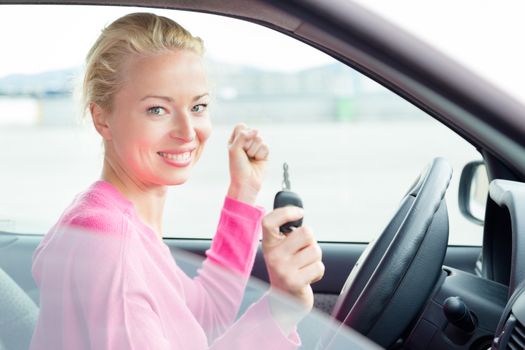 Woman driver showing car keys. Young female driving happy about her new car or drivers license. Caucasian model.