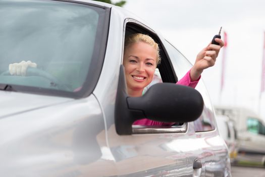 Woman driver showing car keys. Young female driving happy about her new car or drivers license. Caucasian model.