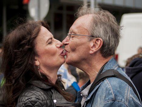 BERLIN, GERMANY - JUNE 21, 2014:Christopher Street Day.Crowd of people participate in the parade celebrates gays, lesbians, bisexuals and transgenders.Prominent in the image a senior couple kissing.