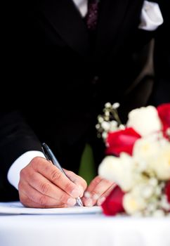 A groom signing his wedding license.  Focus on man's hand.