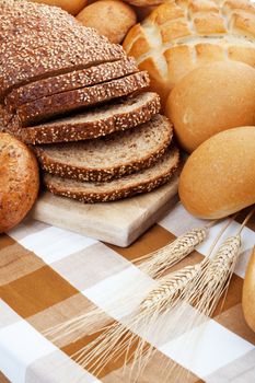 A variety of freshly baked breads along with three stocks of wheat.  Shallow depth of field.