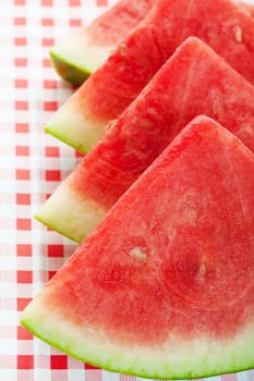 Four watermelon wedges on a red, checkered picnic table cloth.  Shallow depth of field.