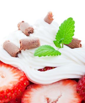 Delicate milk chocolate curls and a sprig of lemon balm garnish fresh strawberries piled high with whipped cream.  Shot on white background with shallow depth of field. Macro. 
