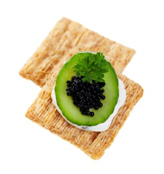 Beautifully textured whole wheat crackers with goat cheese and fresh cucumber, topped with parsley and black beluga caviar.  Shot on white background.