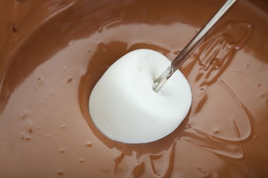 A marshmallow that has just been freshly dipped in warm milk chocolate fondue.  Shot on white background.