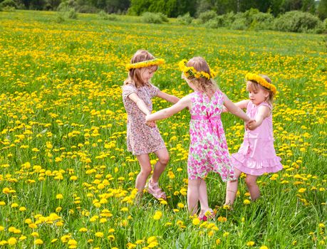 Three little girls wearing dandelion wreath enjoying a summer day outdoors