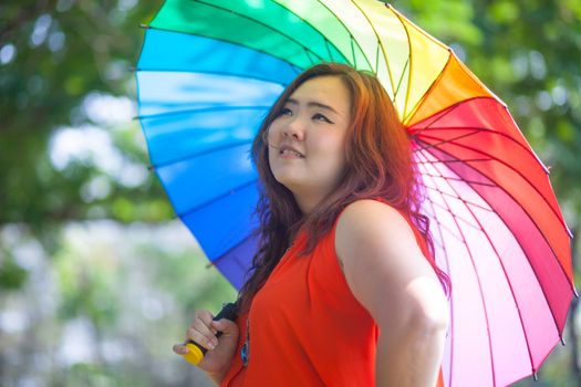 Happy fatty asian woman with umbrella outdoor in a park