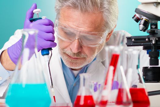 Focused senior life science professional pipetting solution on micro chip.  Lens focus on the researcher's face.