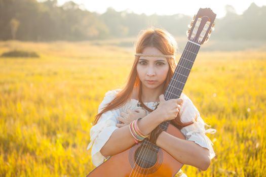 Hippie woman in golden field with acoustic guitar