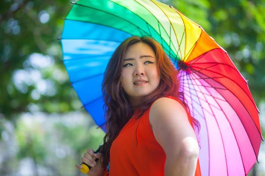 Happy fatty asian woman with umbrella outdoor in a park